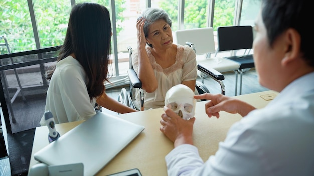 写真 診察室で年配の女性患者の頭蓋骨の異常を診断し、説明する男性医師