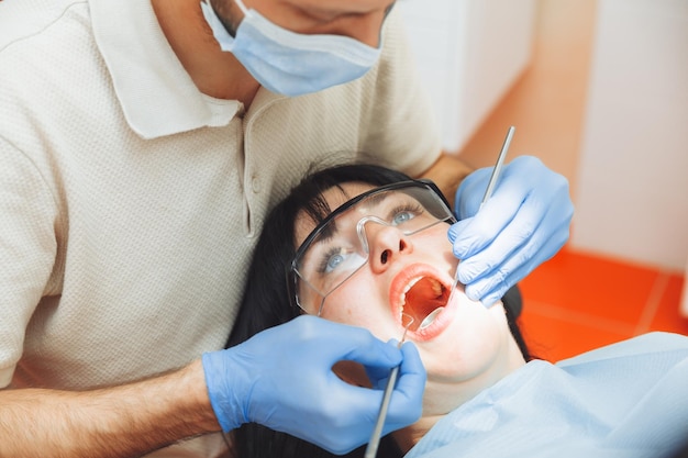 A male doctor examines the oral cavity of a young patient\
sitting in a dentist\'s chair in the office next to the dentist the\
concept of healthy teeth