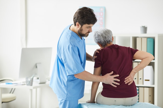 Male doctor examining the back of senior woman during her visit at hospital