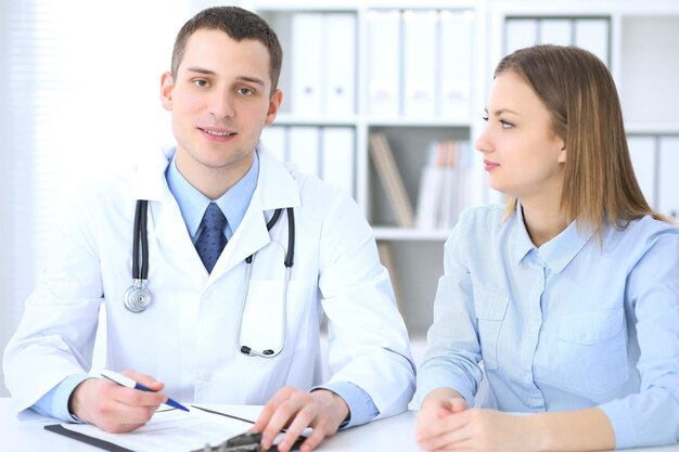 Male doctor and female patient sitting at the table in medical cabinet