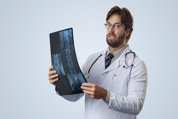Мужчина-врач на сером фоне, глядя на рентгеновский снимок.