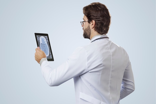 Male doctor on a gray wall looking at a tablet