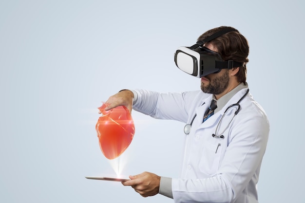 Male doctor on a gray wall using a Virtual Reality Glasses, looking at a virtual heart