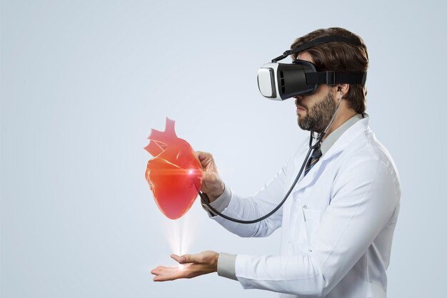 Male doctor on a gray wall using a Virtual Reality Glasses, looking at a virtual heart