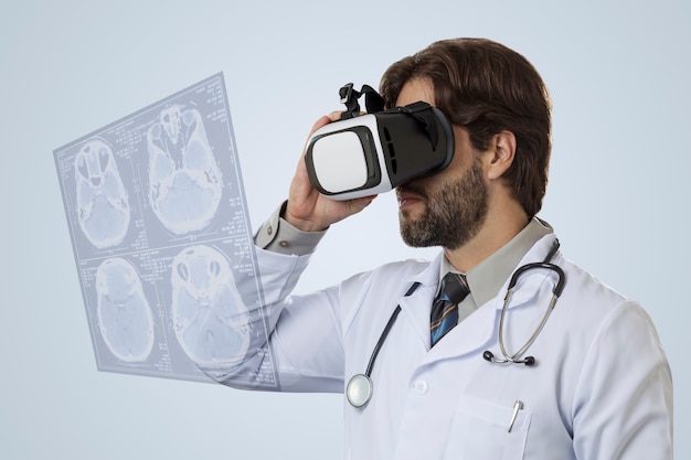 Male doctor on a gray wall, using a Virtual Reality Glasses, looking at a virtual Screen