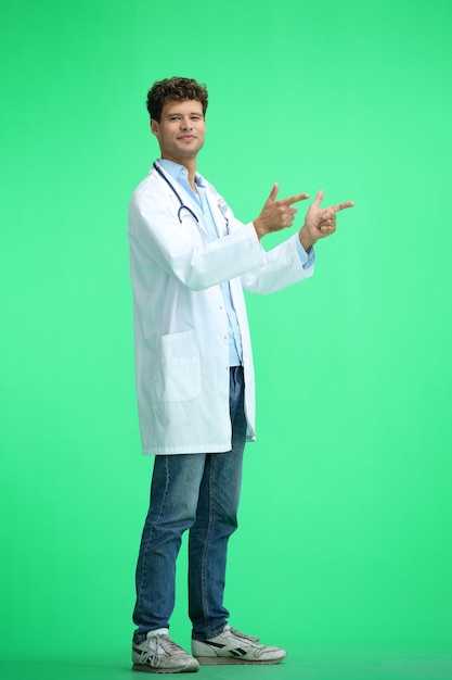 The male doctor on a green background in full height points to the side