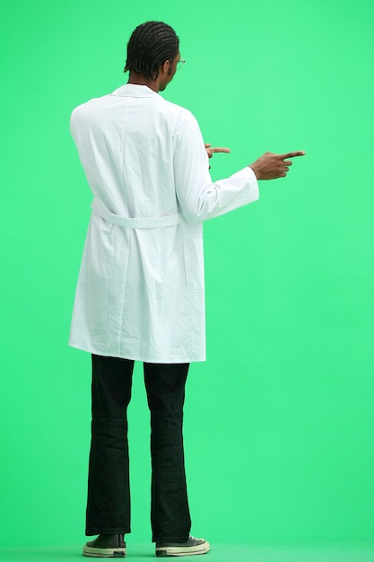 Photo the male doctor on a green background in full height points to the side