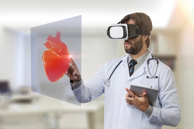 Foto medico maschio nel suo ufficio, utilizzando occhiali per realtà virtuale, guardando un cuore virtuale