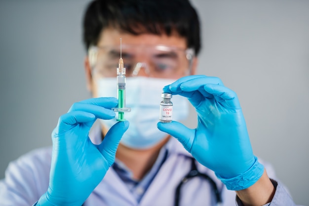 Male doctor holding Coronavirus (Covid-19) vaccine bottle and syringe injection medicine