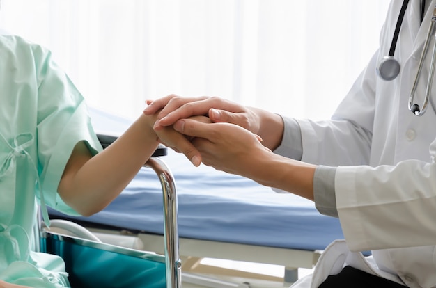 Male Doctor holding female patient hand for encouragement in hospital room. Patient gest depressed, stress, sad.