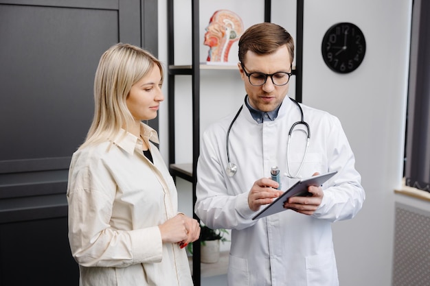 Male doctor holding in hand an aerosol inhaler on a demonstration to a female patient at his office