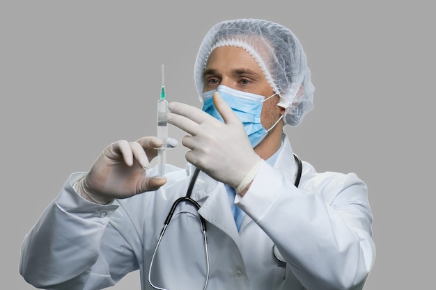 Врач-мужчина держит шприц с инъекцией. Кавказский врач держит шприц на сером фоне. Лечебная вакцина от коронавируса.