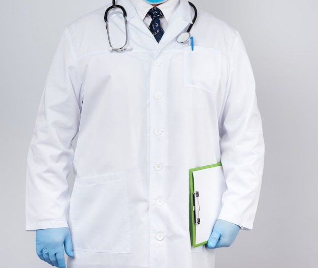 写真 白衣の男性医師、青いラテックス手袋、首に掛かっている聴診器、緑色の紙ホルダーを保持している医師