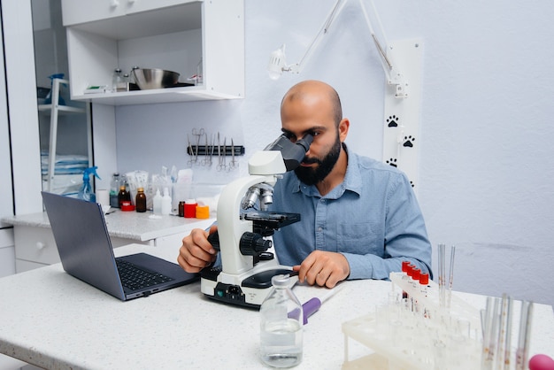 Un medico maschio in laboratorio studia virus e batteri al microscopio. ricerca di virus e batteri pericolosi.