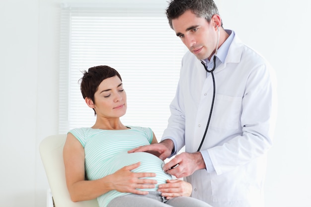 Male Doctor listening into the belly with a stethoscope in a room