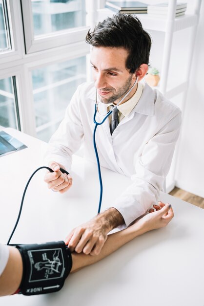 Foto medico maschio che misura pressione sanguigna del paziente con lo stetoscopio