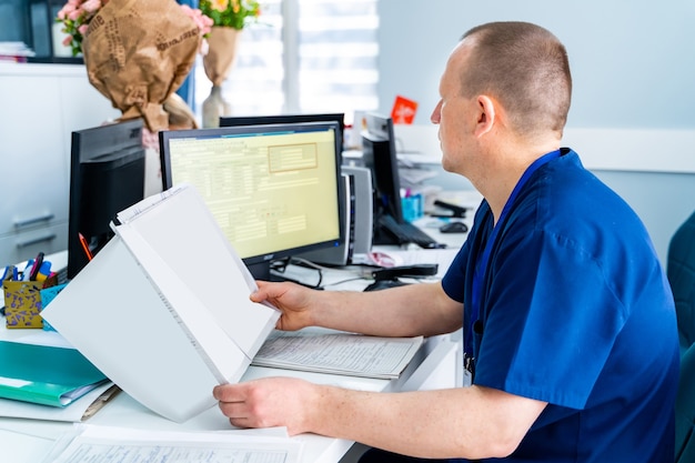 Male doctor in office looking at monitor. Reading results. Modern hospital office background.