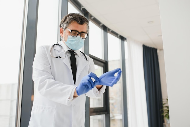 Foto il medico maschio con una maschera protettiva indossa i guanti in clinica