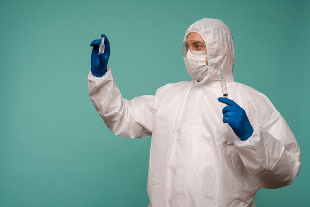 A male doctor in protective overalls and a mask holds an ampoule with a vaccine and syringe in his hands. Coronovirus protection concept in China. 