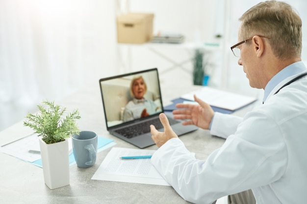 Male doctor providing online consultation to old woman in clinic