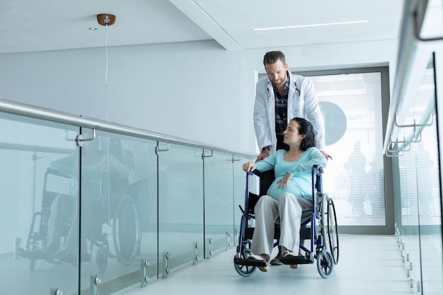 Male doctor pushing pregnant woman on wheelchair in the corridor