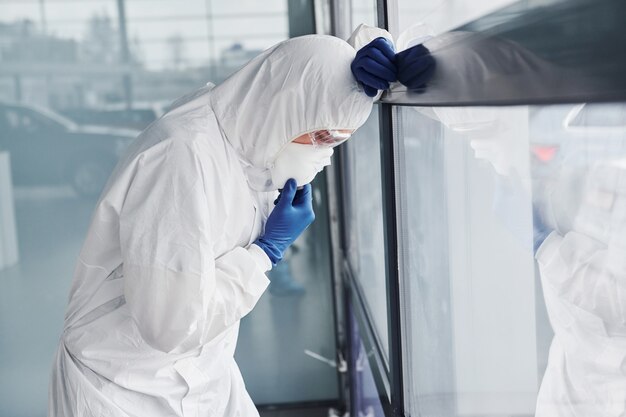 Scienziato medico maschio in camice da laboratorio, occhiali difensivi e maschera si sente male, esausto e malato