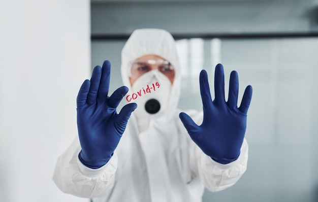 male doctor scientist in lab coat, defensive eyewear and mask holds glass with covid-19 word on it