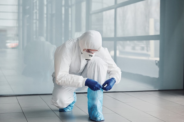 Male doctor scientist in lab coat, defensive eyewear and mask wearing protective material on legs