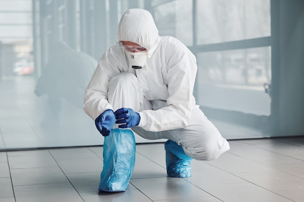 Male doctor scientist in lab coat, defensive eyewear and mask wearing protective material on legs