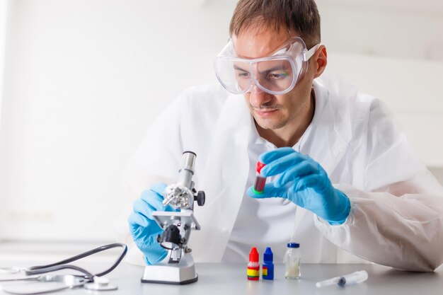 A male doctor or scientist looking through a microscope on a table with laptop computer in background