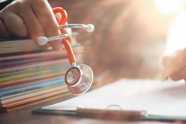 Male doctor search information in book and writtnig prescription medical stethoscope on the desk at clinic Medical knowledge and education concept