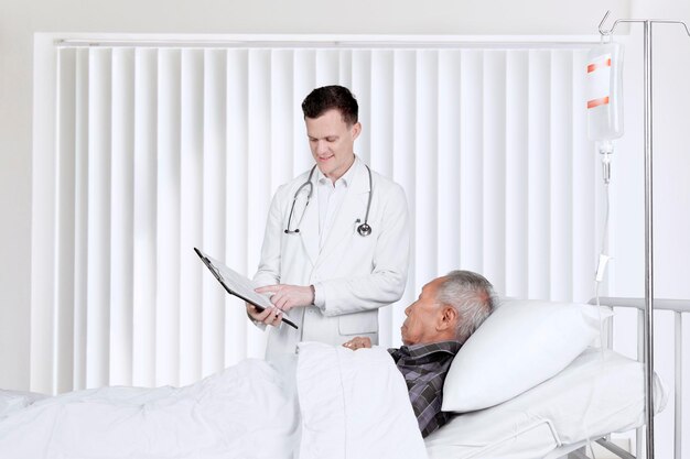 Photo male doctor showing a medical report on the clipboard to his elderly male patient on the bed. shot in the patient room