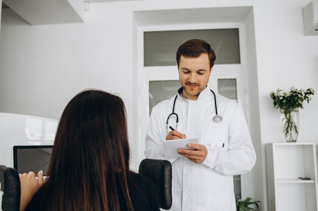 Photo male doctor showing to unrecognizable female patient problem with vertebra on special model sitting at table with computer in modern office