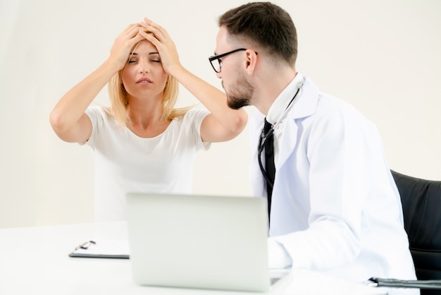 Male doctor talks to female patient in hospital office while looking at data on laptop computer.