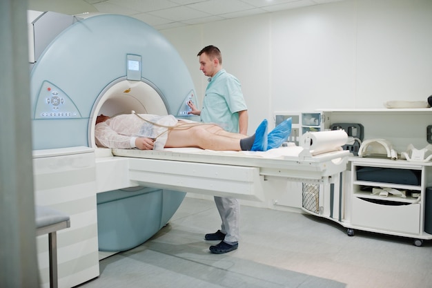 Врач-мужчина включает аппарат магнитно-резонансной томографии с пациентом внутри