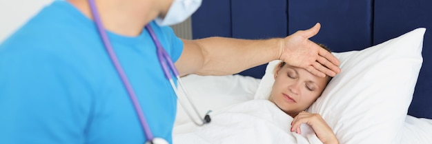 制服を着た男性医師がベッド熱に横たわっている患者の体温をチェックし、自宅の医師に電話し、