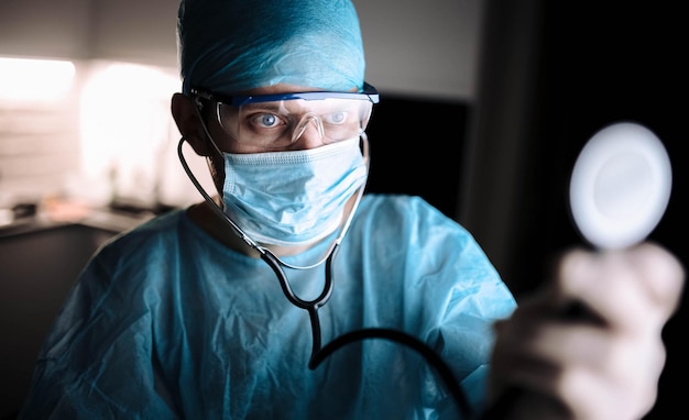 врач-мужчина в форме и очках со стетоскопом в легкие пациента