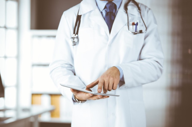 Male doctor using tablet computer in clinic, close-up. Perfect medical service in hospital. Medicine and healthcare concept.