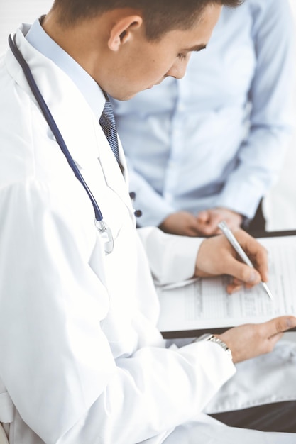 Male doctor using touchpad or tablet pc while consulting female patient in hospital. Medicine and healthcare concept.