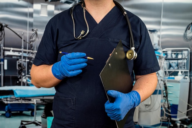 Male doctor wear in dark blue uniform gloves holding a clipboard for record in the info card of the patient in modern hospital healthcare concept