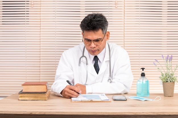 A male doctor  Wear white adhesive clothes sits at his desk.