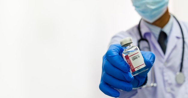 白い背景にcovid 19ワクチンウイルスのボトルを保持している制服の医療用手袋を身に着けている男性医師コピースペース