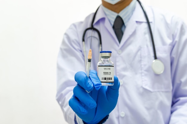 白い背景にcovid 19ワクチンウイルスのボトルを保持している制服の医療用手袋を身に着けている男性医師コピースペース