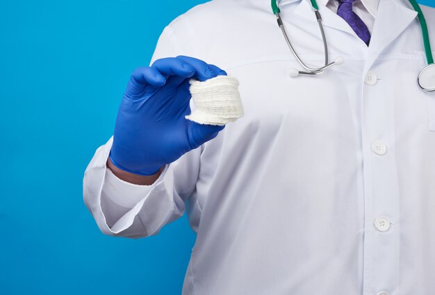 Male doctor in a white coat, blue latex medical gloves holding a stack of cotton cosmetic discs