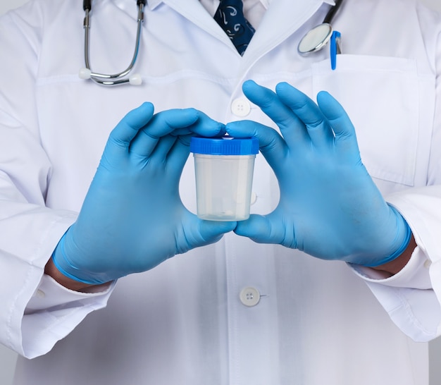 Male doctor in a white coat and tie stands and holds a plastic container for urine specimen