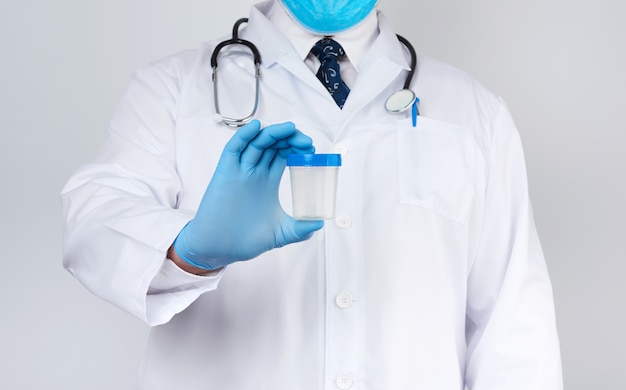 Male doctor in a white coat and tie stands and holds a plastic container for urine specimen