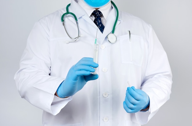 Male doctor in a white coat and tie stands and holds a plastic syringe with a needle