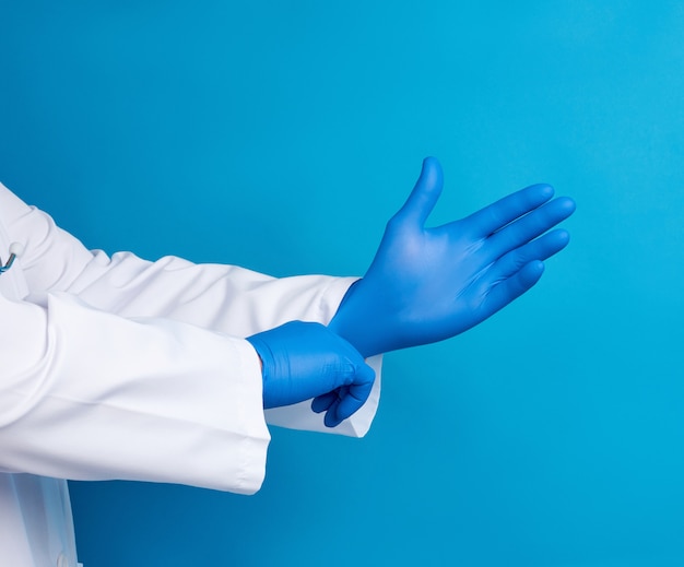 Medico maschio in uniforme bianca indossa le mani guanti di lattice sterili blu