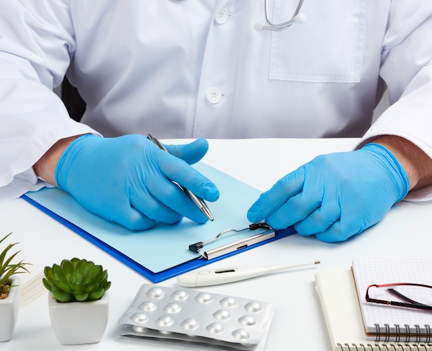 Male doctor in a white uniform sits at a white table and writes in a paper notebook