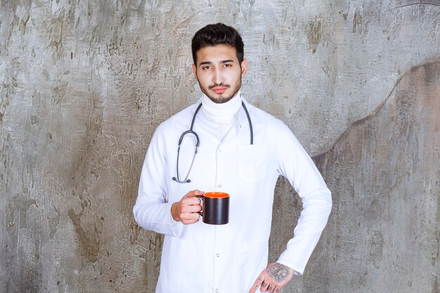 Male doctor with stethoscope holding a cup of coffee